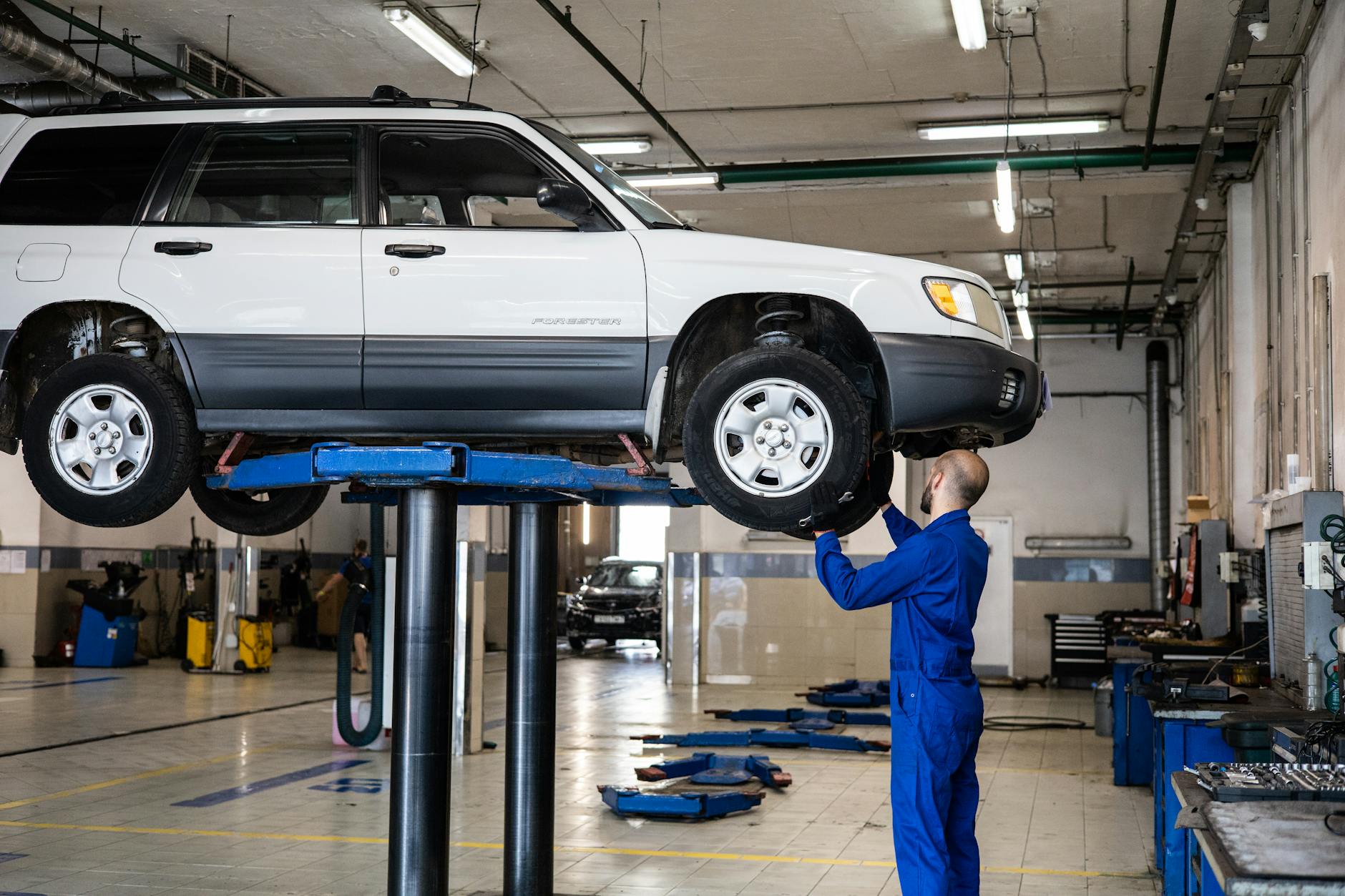 Kiedy wymiana klocków a kiedy pełny serwis hamulców w ciężkim i szybkim SUV-ie premium Mechanik sprawdza hamulce białego SUV-a na podnośniku w warsztacie