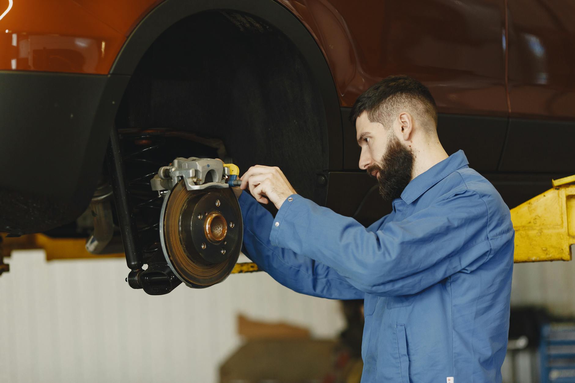 Mechanik w niebieskim kombinezonie naprawia hamulce w nowoczesnym warsztacie