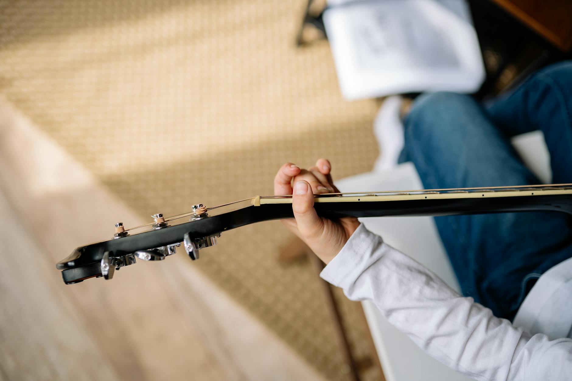 Osoba w białej koszuli ćwiczy akordy na gitarze akustycznej