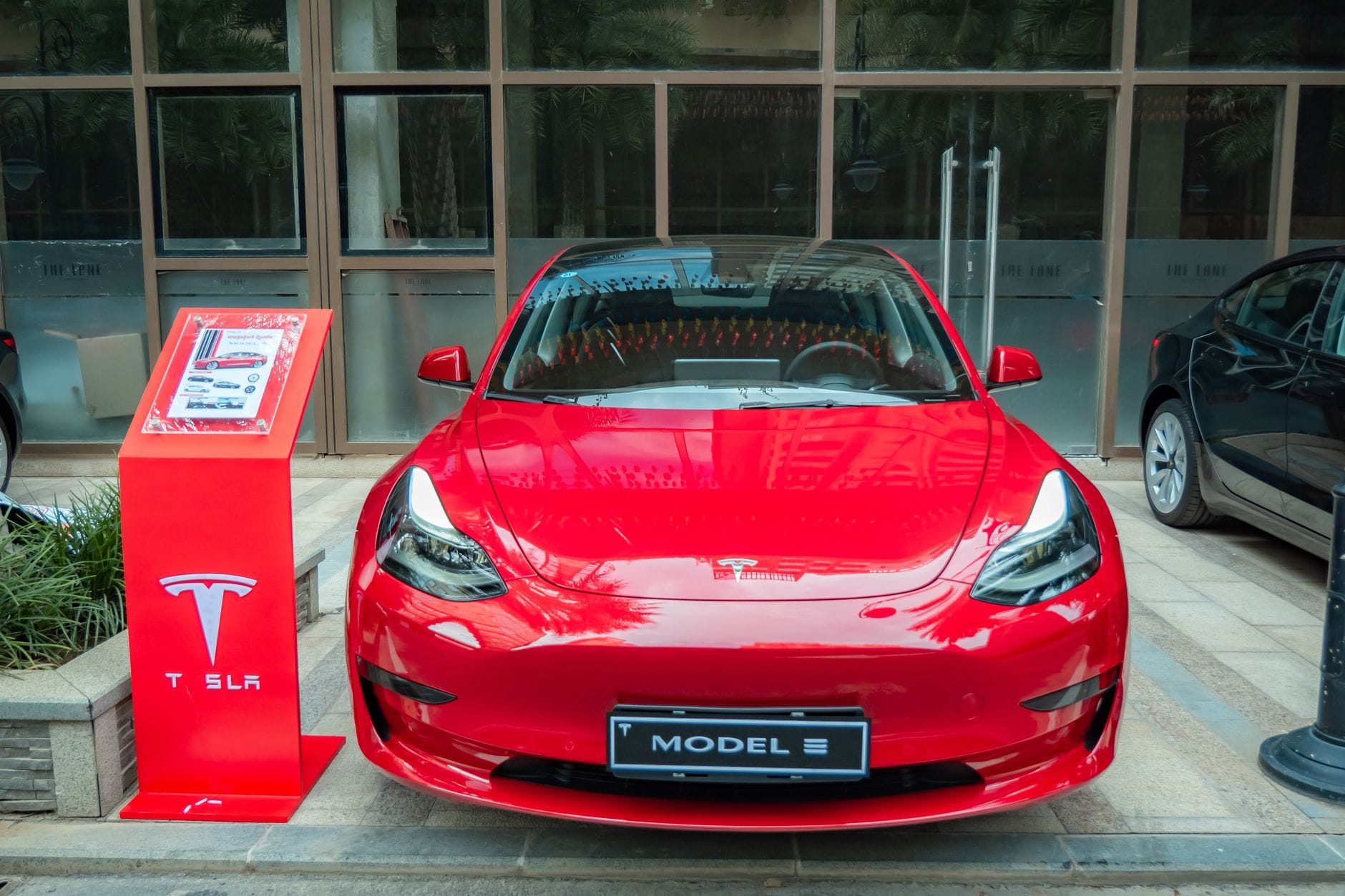 Czy sportowe auto pasuje do stylu eko jak łączyć pasję z rozsądkiem i planetą Czerwony Tesla Model 3 zaparkowany w nowoczesnej miejskiej przestrzeni