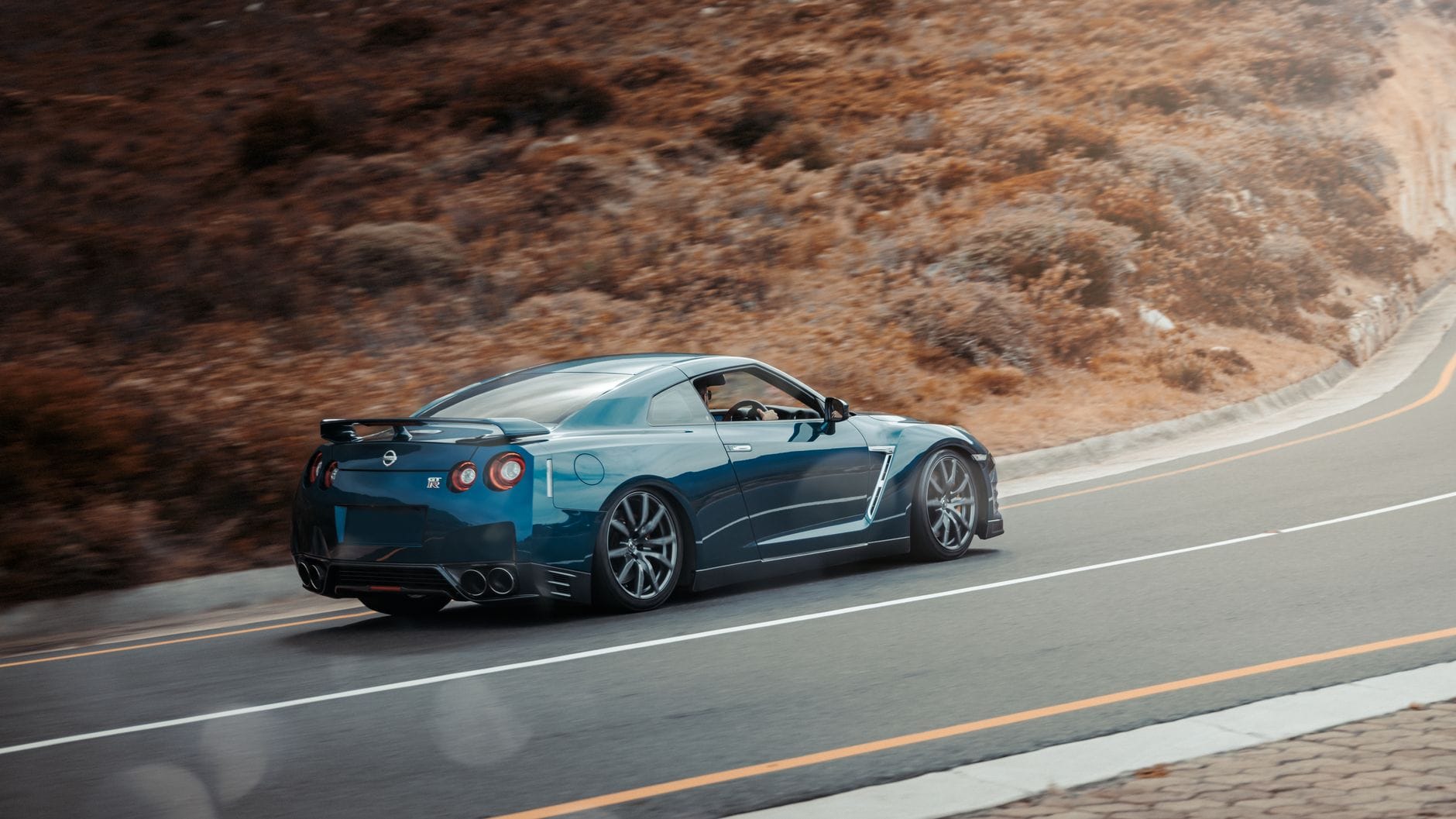 Niebieski Nissan GT-R pędzi malowniczą drogą