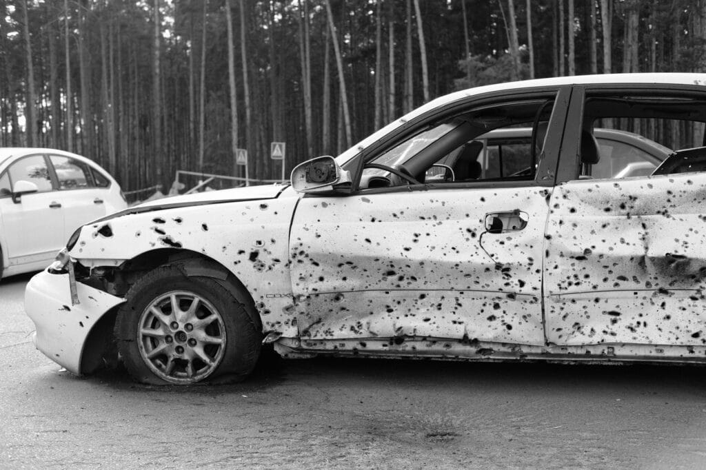 Czarno-białe auto z przestrzelinami porzucone w lesie