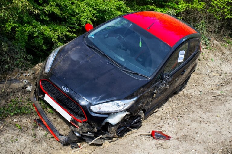 Uszkodzony czarno-czerwony Ford Fiesta porzucony przy drodze